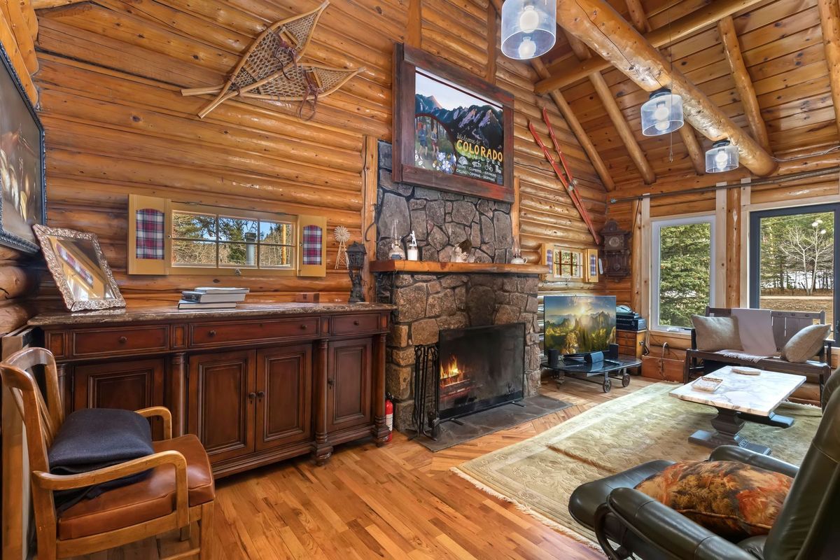 A remodeled log interior with a stone fireplace, vaulted ceiling, and river-facing windows
